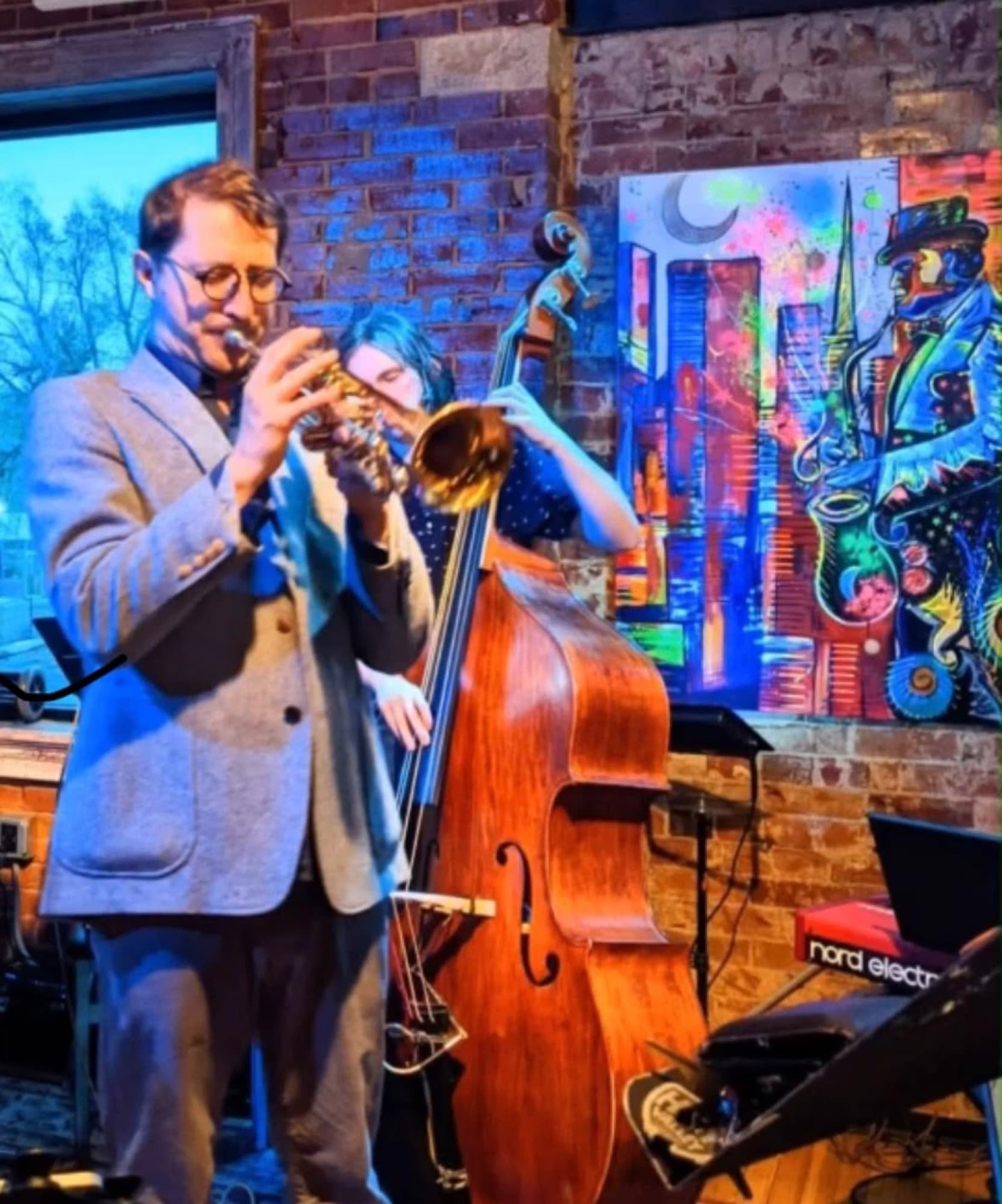 Reid Poole playing trumpet beside an upright bassist and colorful jazz artwork